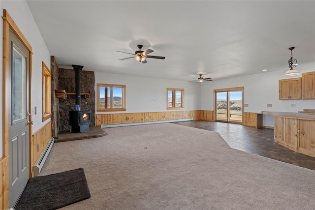 53 Skyview Ln, Townsend, MT 59644 - unfurnished living room with baseboard heating, a wood stove, wainscoting, a ceiling fan, and wood walls