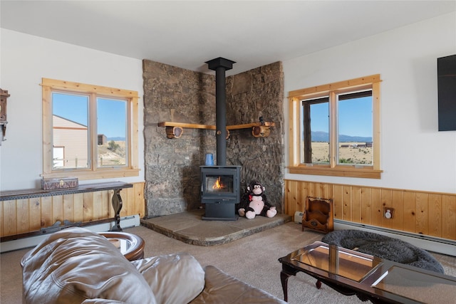 53 Skyview Ln, Townsend, MT 59644 - carpeted living room featuring a wood stove, healthy amount of natural light, a baseboard heating unit, wainscoting, and wooden walls