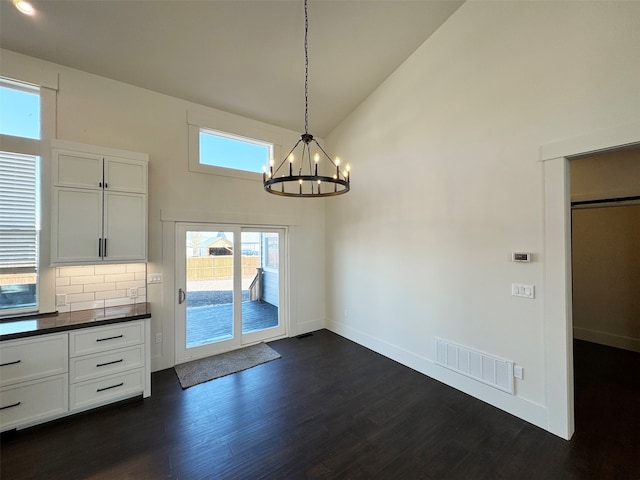 unfurnished dining area with high vaulted ceiling, a notable chandelier, and dark wood-type flooring