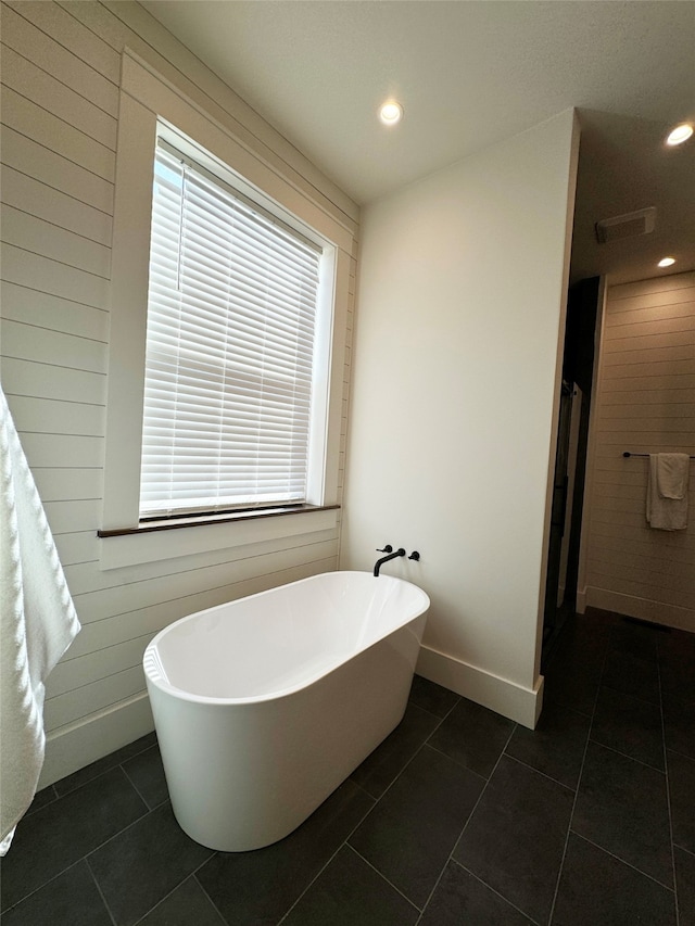 bathroom featuring wooden walls, tile patterned floors, and a washtub