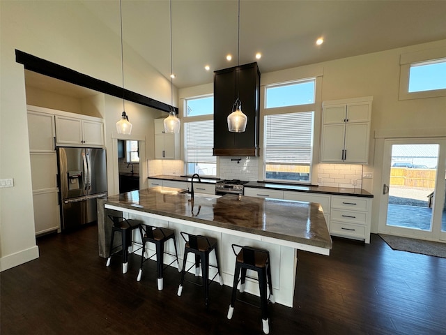 kitchen featuring a center island with sink, stainless steel appliances, plenty of natural light, and dark wood-type flooring