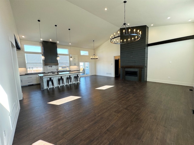 living room with a chandelier, dark hardwood / wood-style flooring, high vaulted ceiling, and a large fireplace