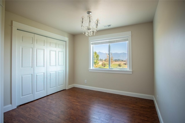 unfurnished bedroom featuring a closet, baseboards, an inviting chandelier, and dark wood-style floors