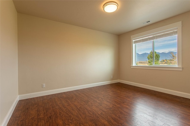 unfurnished room with dark wood-style flooring, visible vents, and baseboards
