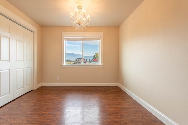 unfurnished bedroom featuring dark wood-type flooring, a closet, an inviting chandelier, and baseboards