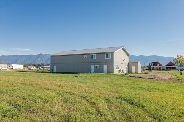 rear view of house with a mountain view, a pole building, metal roof, a lawn, and an outbuilding