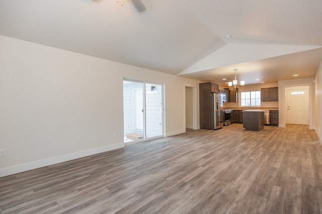 unfurnished living room with hardwood / wood-style floors, vaulted ceiling, sink, and ceiling fan with notable chandelier