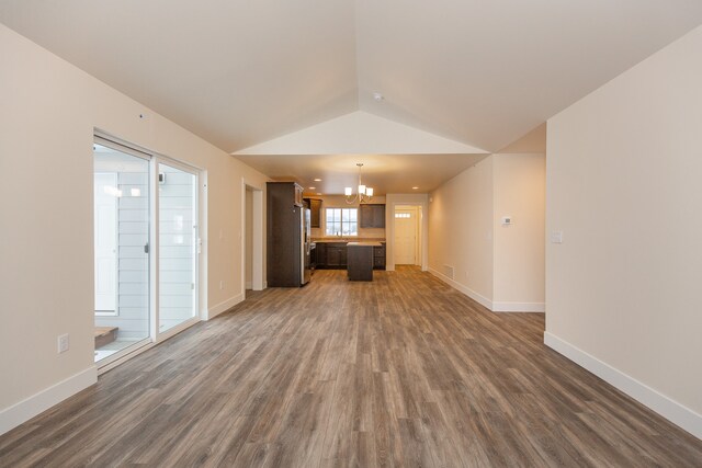 unfurnished living room featuring dark wood-type flooring, vaulted ceiling, and an inviting chandelier