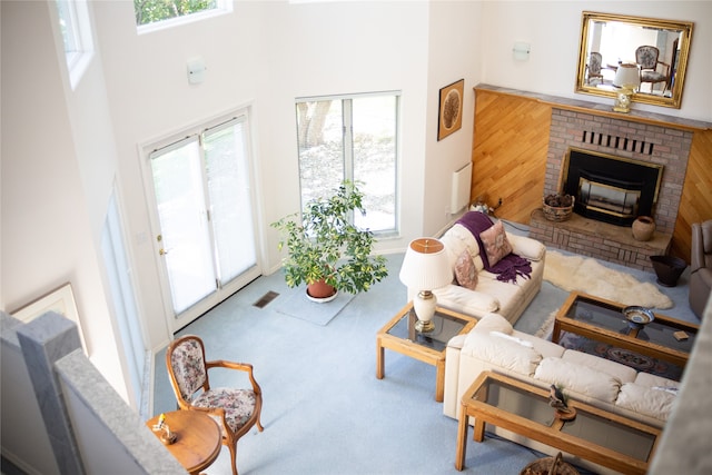 living room with a brick fireplace, a towering ceiling, plenty of natural light, and light wood-type flooring