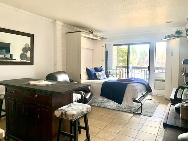 tiled bedroom featuring a textured ceiling, ornamental molding, an AC wall unit, and access to exterior