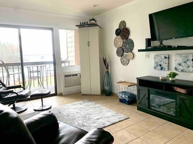 tiled living room with crown molding and an AC wall unit