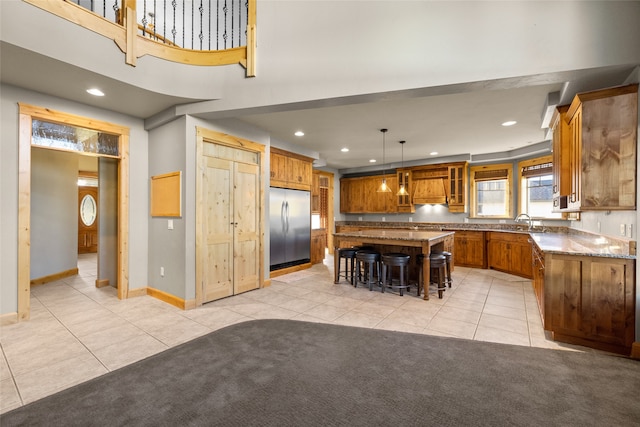 kitchen with stainless steel built in refrigerator, a breakfast bar, a center island, decorative light fixtures, and light stone countertops