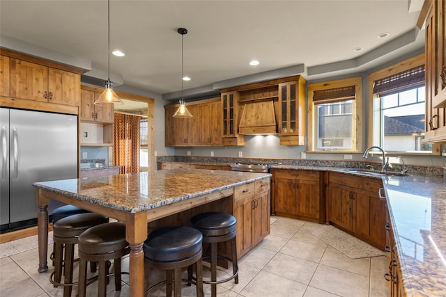 kitchen with pendant lighting, built in refrigerator, custom range hood, a kitchen island, and dark stone countertops