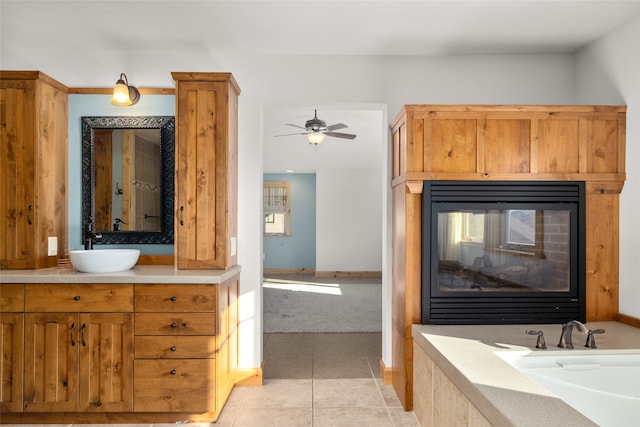 bathroom with a multi sided fireplace, a tub to relax in, vanity, tile patterned flooring, and ceiling fan