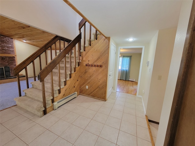 staircase with wooden ceiling, a brick fireplace, tile patterned flooring, a baseboard heating unit, and wood walls