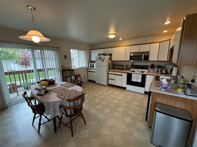 kitchen featuring white appliances, hanging light fixtures, white cabinets, and sink