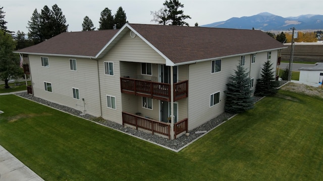 rear view of house featuring a balcony, a lawn, and a mountain view