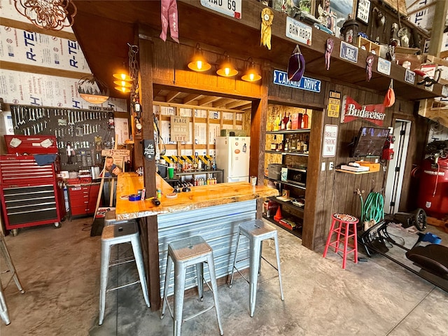 interior space with wooden walls, white refrigerator, a workshop area, and concrete floors