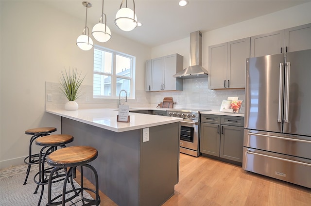 kitchen with a breakfast bar, decorative light fixtures, sink, premium appliances, and wall chimney range hood