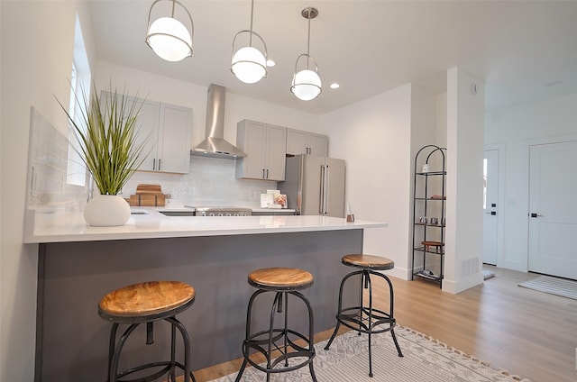 kitchen with decorative light fixtures, high end refrigerator, a kitchen breakfast bar, and wall chimney exhaust hood