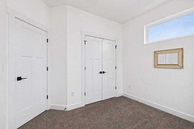 unfurnished bedroom featuring baseboards, dark colored carpet, and a closet