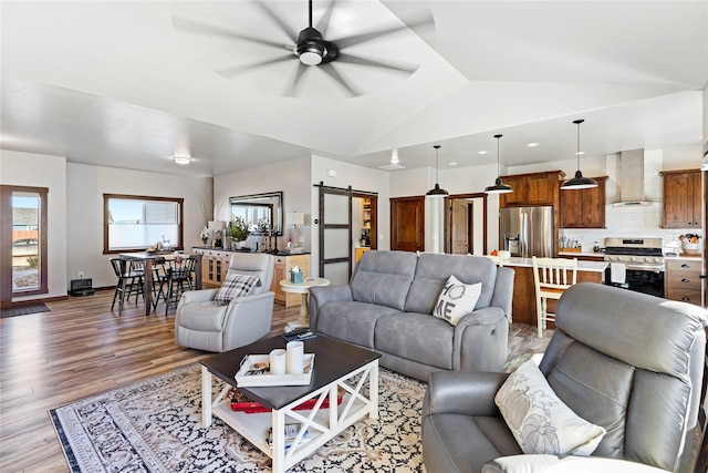 living room featuring ceiling fan, a barn door, wood-type flooring, and vaulted ceiling