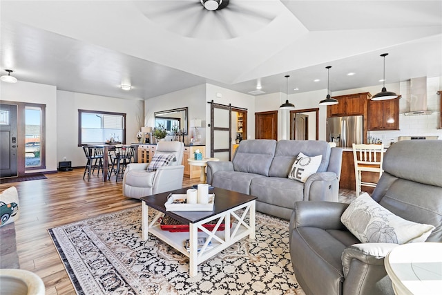 living room with lofted ceiling, a barn door, light wood-type flooring, and ceiling fan