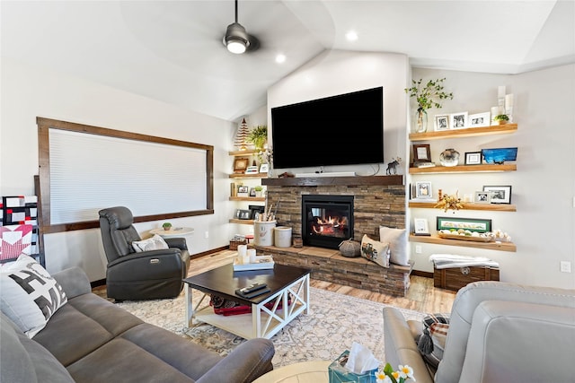 living room featuring ceiling fan, a stone fireplace, light hardwood / wood-style flooring, and vaulted ceiling