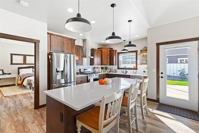 kitchen featuring hanging light fixtures, wall chimney range hood, a breakfast bar, a kitchen island, and appliances with stainless steel finishes