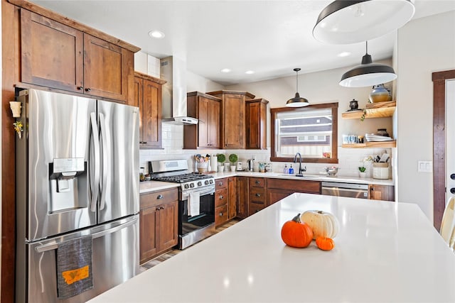 kitchen with wall chimney range hood, sink, hanging light fixtures, decorative backsplash, and appliances with stainless steel finishes