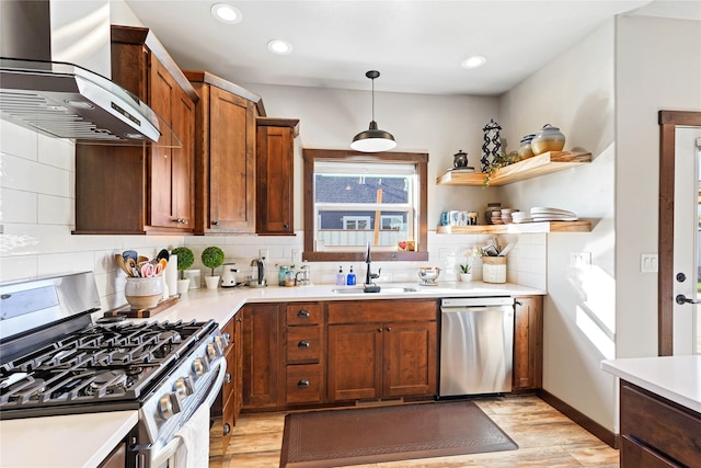 kitchen featuring pendant lighting, wall chimney range hood, sink, light hardwood / wood-style flooring, and appliances with stainless steel finishes