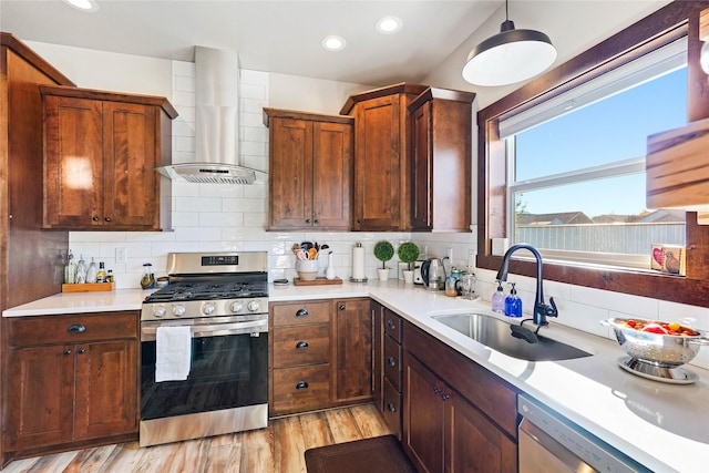 kitchen featuring sink, hanging light fixtures, wall chimney exhaust hood, light wood-type flooring, and stainless steel appliances