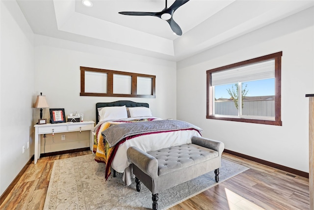 bedroom with ceiling fan, a raised ceiling, and light hardwood / wood-style flooring