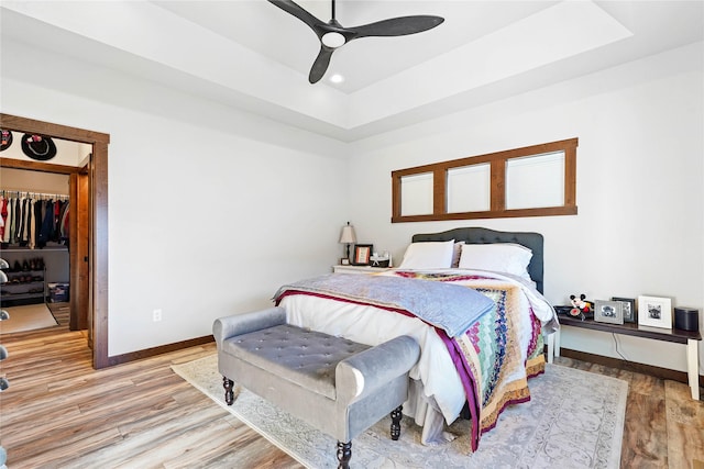 bedroom featuring ceiling fan, a spacious closet, a raised ceiling, hardwood / wood-style floors, and a closet