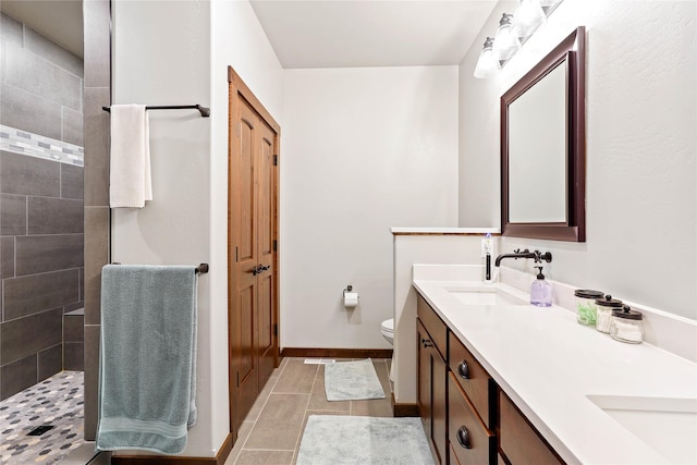 bathroom featuring toilet, a tile shower, vanity, and tile patterned floors