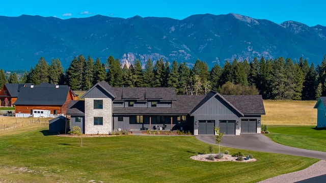 view of front of home with stone siding, an attached garage, a mountain view, board and batten siding, and a front yard