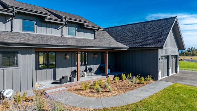 modern farmhouse style home with a garage, driveway, a shingled roof, a porch, and board and batten siding