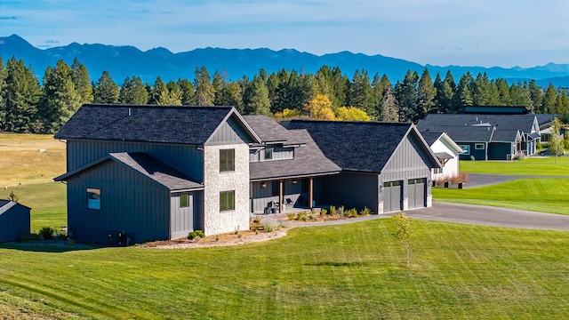 modern inspired farmhouse with driveway, stone siding, a mountain view, and a front yard