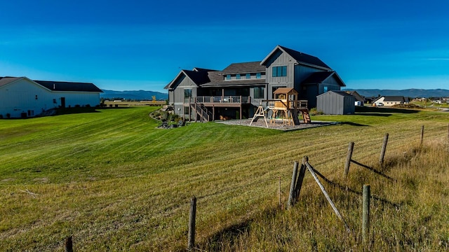 rear view of property featuring board and batten siding, a mountain view, a playground, and a yard