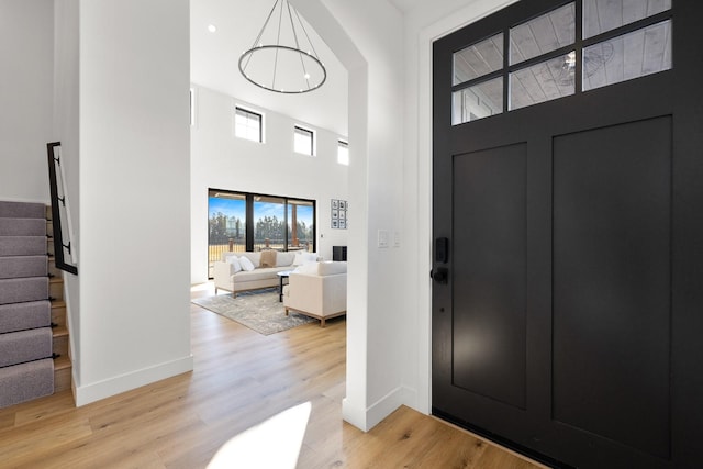 foyer entrance with baseboards, stairway, a towering ceiling, and light wood-style floors