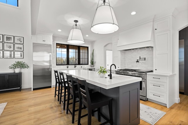 kitchen with high end appliances, arched walkways, white cabinets, and custom range hood