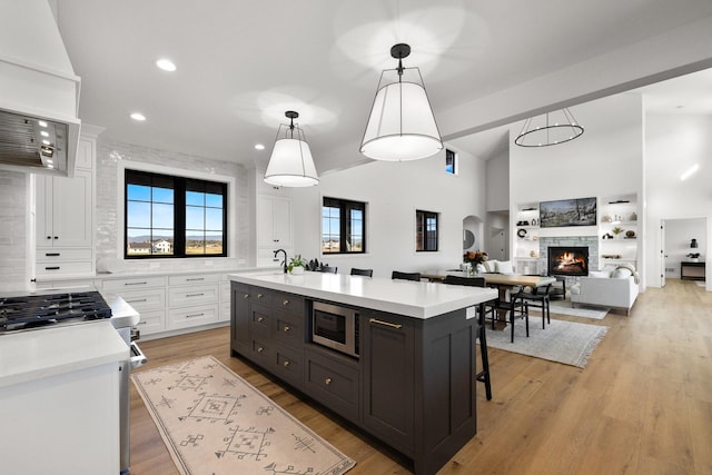 kitchen with a center island with sink, stainless steel microwave, hanging light fixtures, light countertops, and white cabinetry