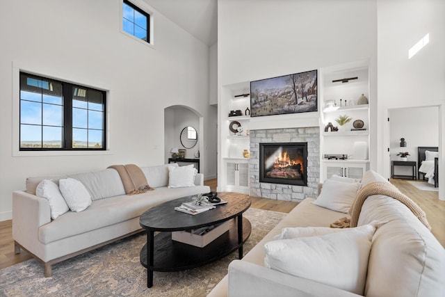 living room featuring built in features, arched walkways, wood finished floors, and a stone fireplace