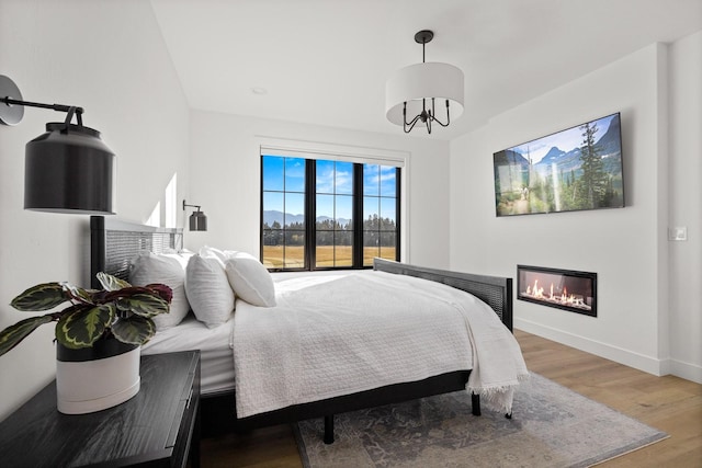 bedroom with baseboards, wood finished floors, and a glass covered fireplace