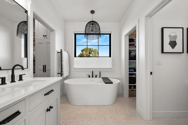 bathroom with a spacious closet, a freestanding tub, vanity, and baseboards