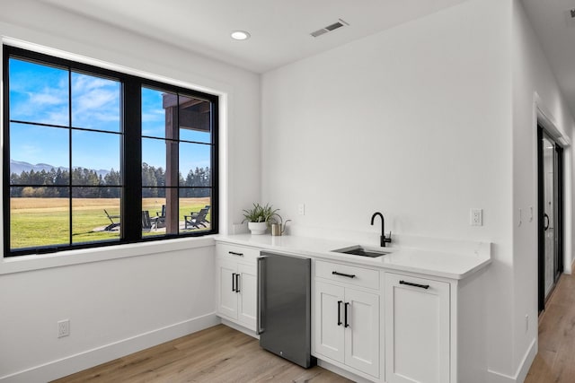 bar featuring a sink, visible vents, baseboards, light wood-style floors, and stainless steel refrigerator