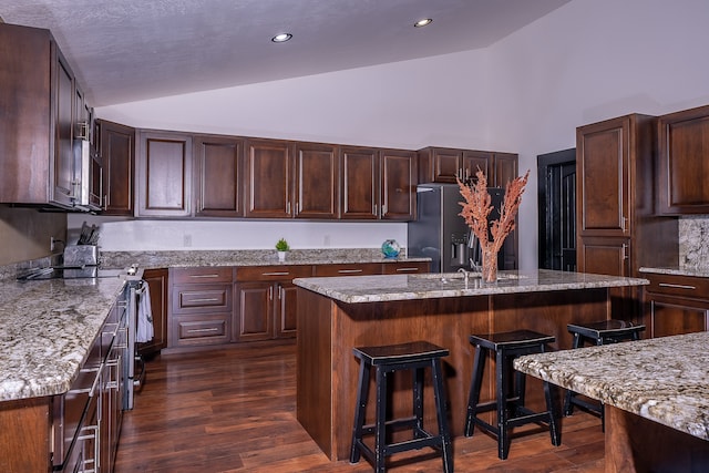 kitchen with light stone countertops, an island with sink, a breakfast bar area, and dark hardwood / wood-style floors