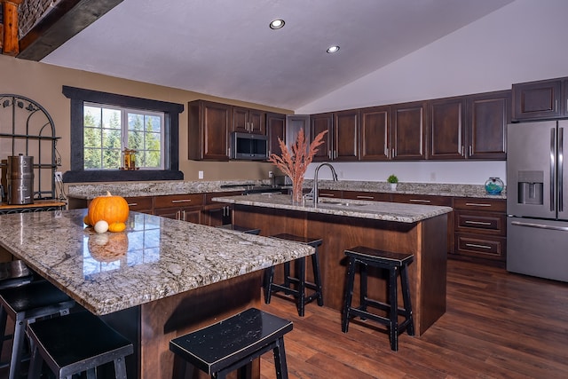 kitchen with lofted ceiling, a kitchen island with sink, dark wood-type flooring, appliances with stainless steel finishes, and a breakfast bar area