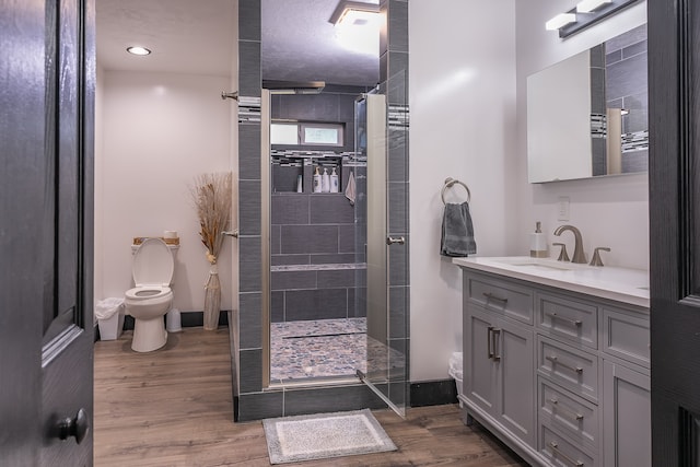 bathroom with vanity, tiled shower, toilet, and hardwood / wood-style flooring