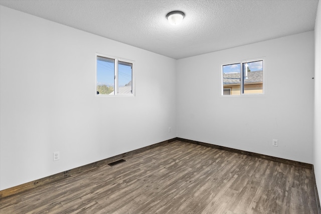 unfurnished room with a textured ceiling, a wealth of natural light, and dark wood-type flooring